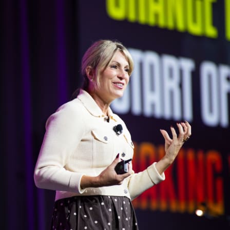A woman speaking on stage with a screen behind her