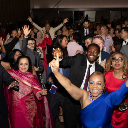 Crowd of people in formal attire extending their arms up high and looking happy