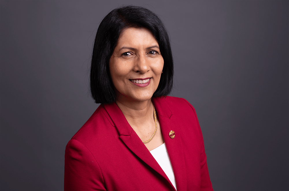 Toastmasters International President Radhi Spear in red suit jacket with Toastmasters pin