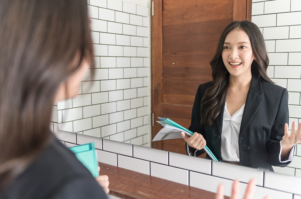 Woman in suit jacket smiling at a mirror