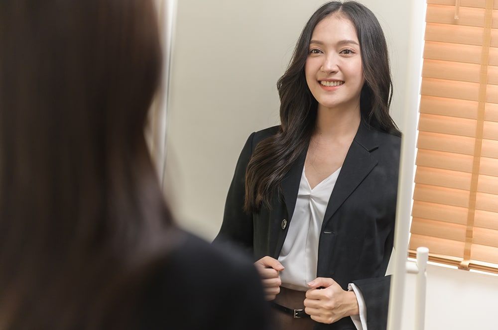 Woman in suit jacket holding papers and looking in mirror