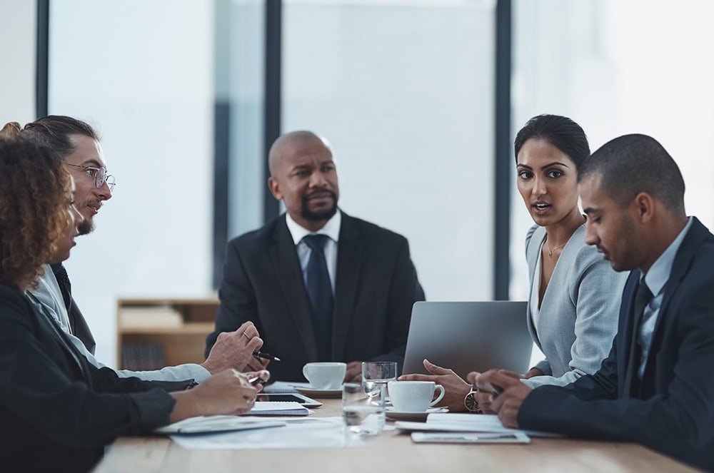 A group of five business professionals speaking together at a table
