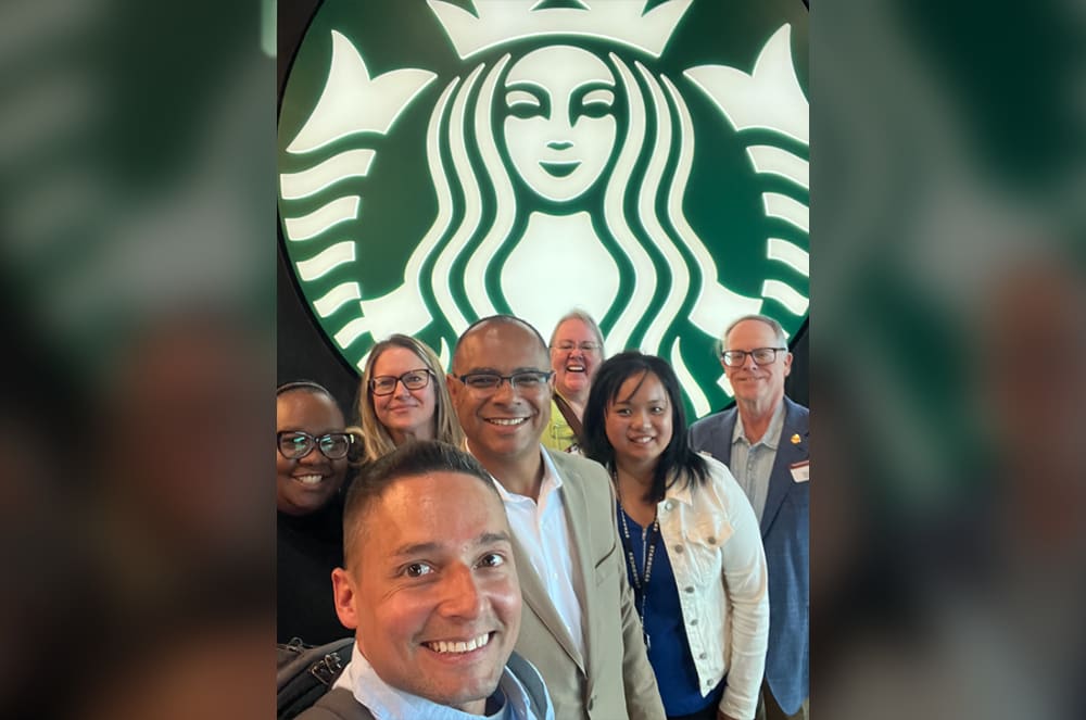 A group of people smiling in front of the Starbucks logo
