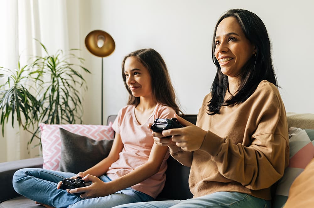 A woman and young girl sitting on a couch playing video games together
