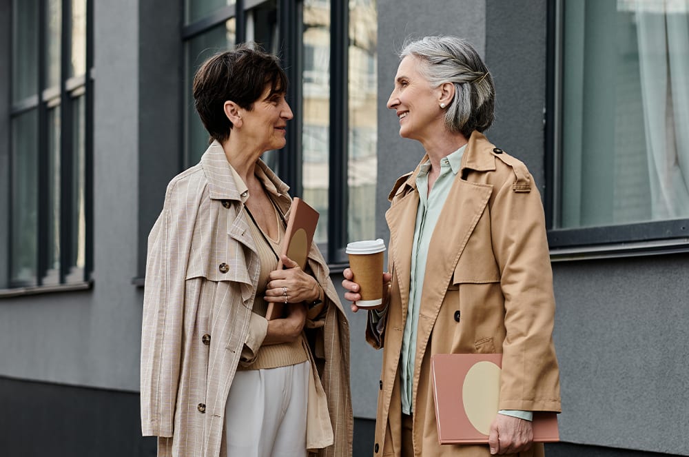 A woman holding a notebook speaking outside to a woman holding a coffee cup