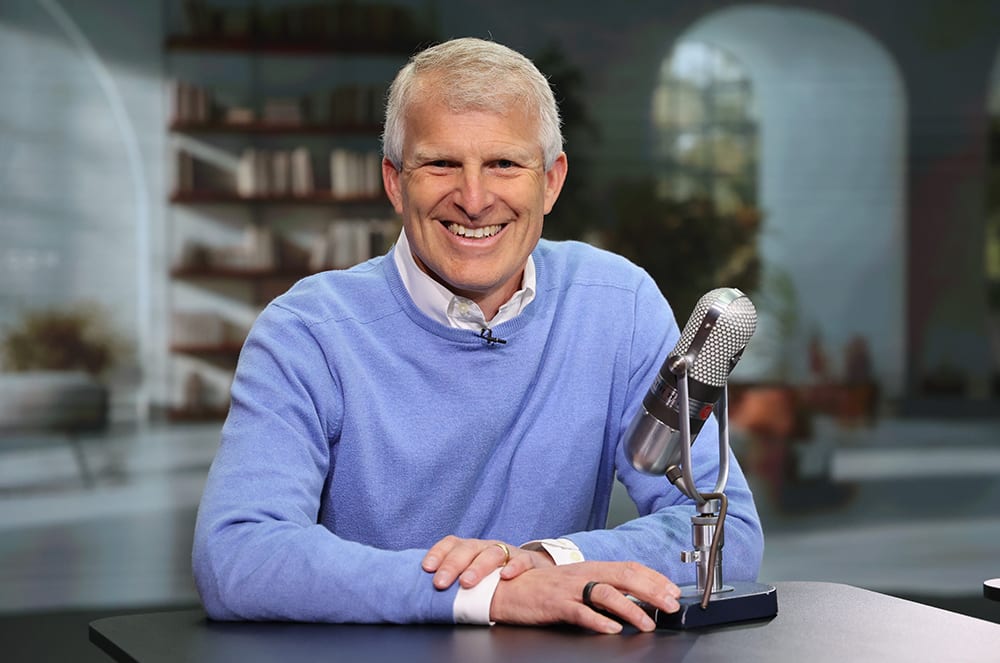 Man in blue long-sleeved shirt smiling next to a microphone
