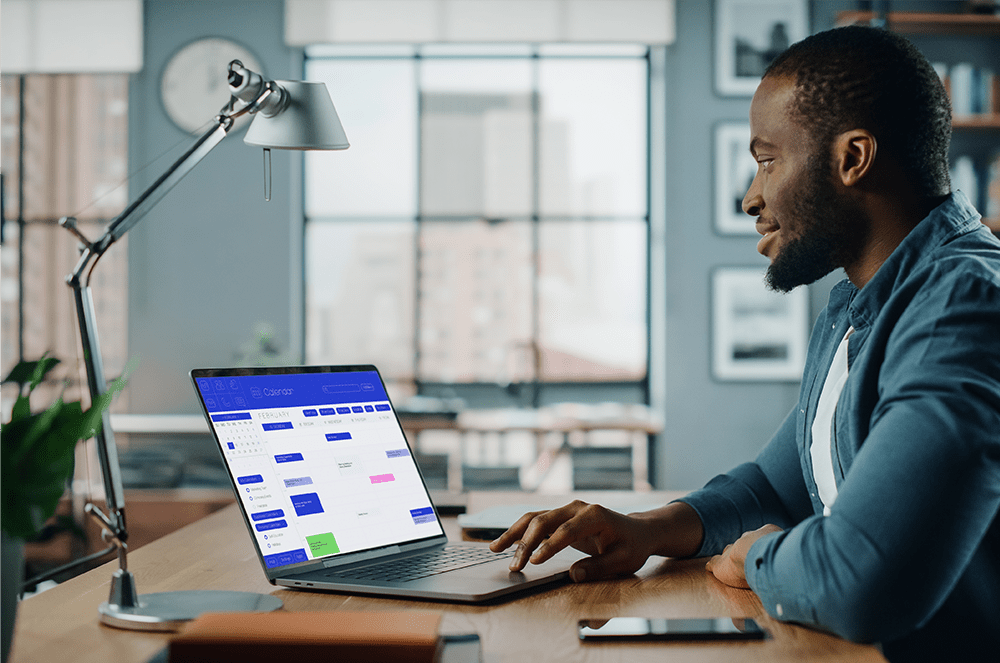 A man sitting at a desk working on a laptop displaying a calendar