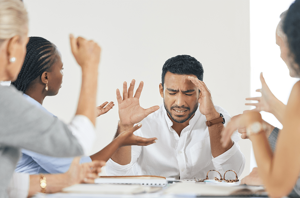 A group of people simultaneously talking to a man with his hands raised and eyes closed