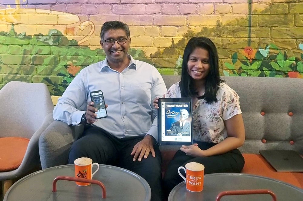 Man and woman sitting down and holding digital copies of the Toastmaster magazine