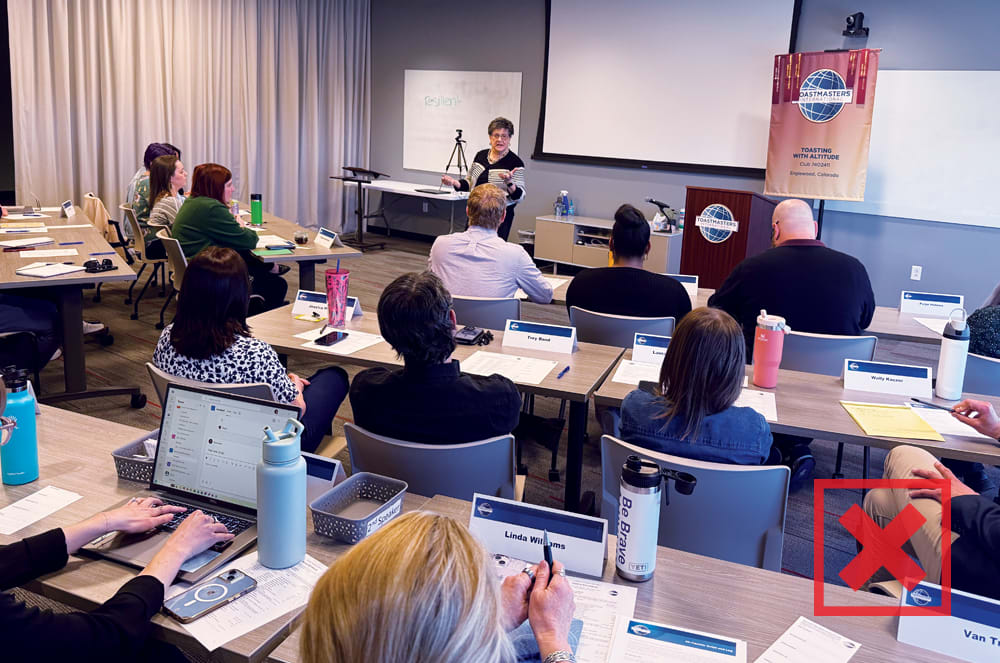 A woman speaking to an audience sitting at desks