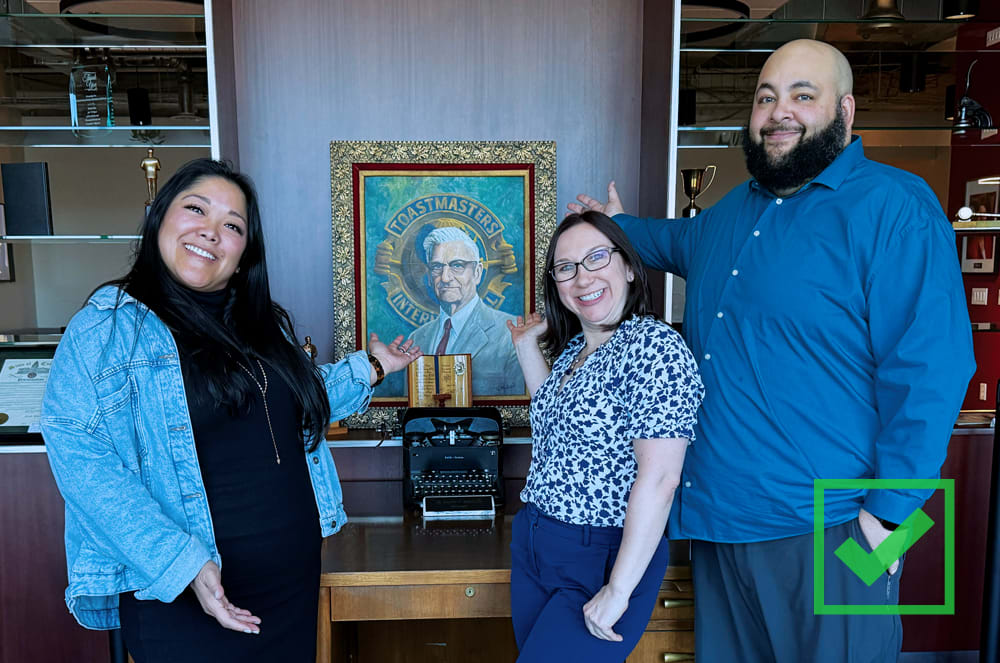 Three people with their arms pointing at a photo of Ralph Smedley