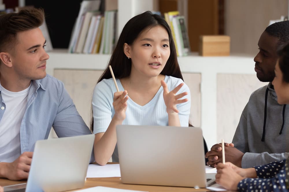 A woman speaking to two people at a table with a laptop