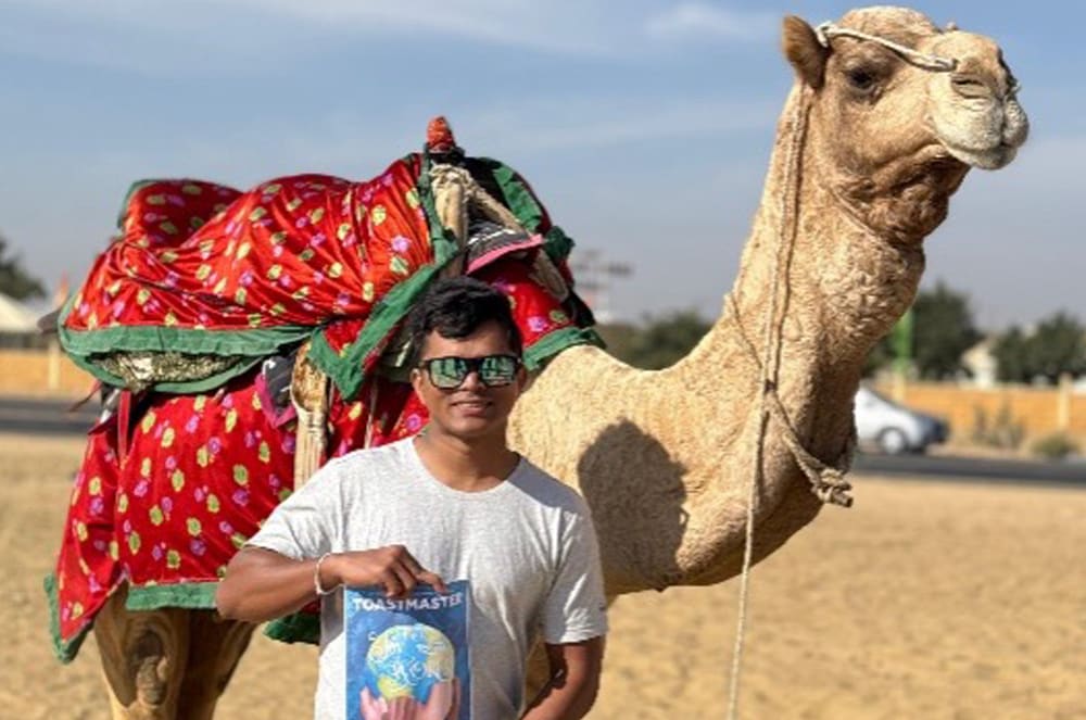 Man holding a printed cover of a magazine standing in front of a camel