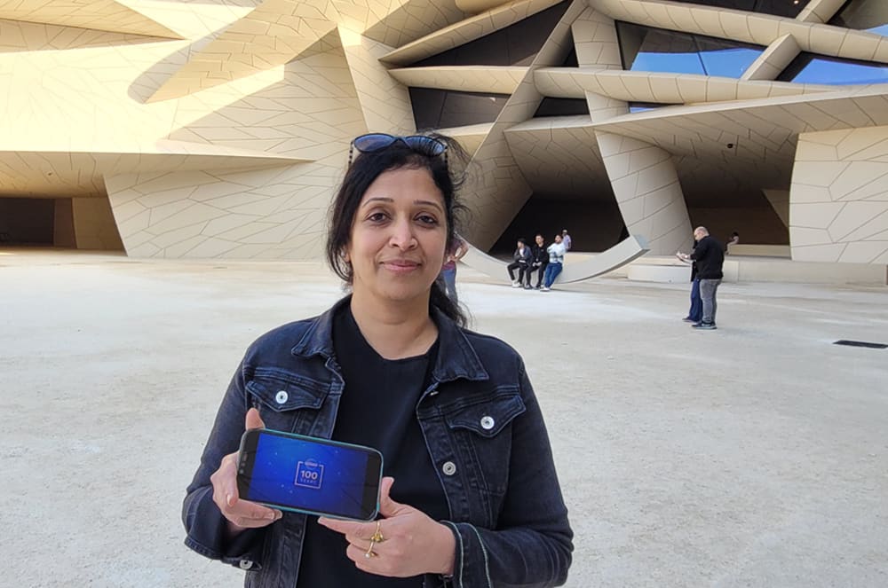 Woman wearing a black jacket showing the Toastmasters International centennial logo on her phone while standing in front of a museum