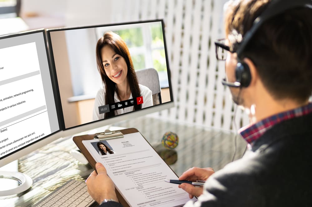 A person holding a clipboard interviewing a woman on a computer