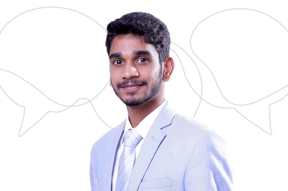 A young man in a white suit stands against a plain white background, with abstract speech bubble shapes surrounding him.