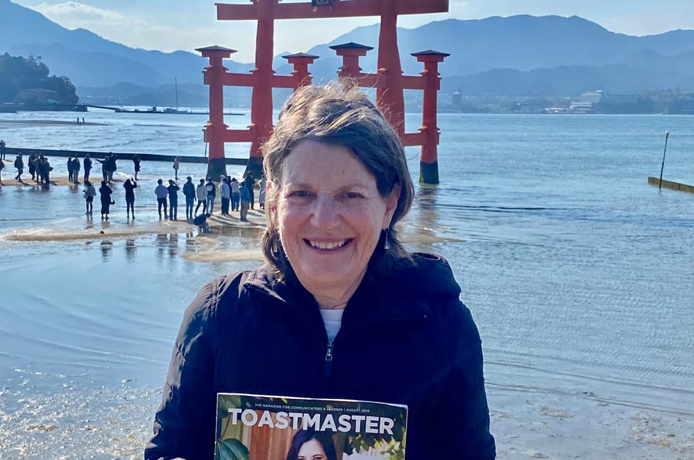 Woman in black jacket posing with a magazine in front of a shrine in water