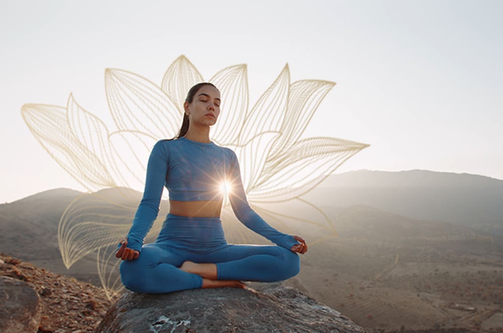 A woman in a blue workout set mediating in a lotus pose on a rock outside