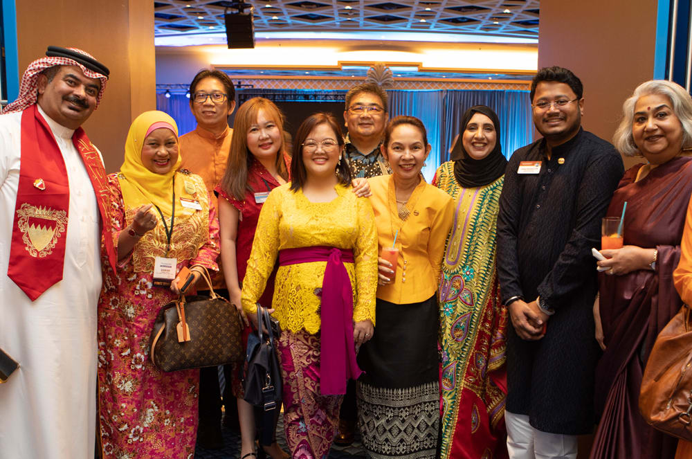 A group of people, dressed in colorful traditional attire, are gathered together in what appears to be a conference or event setting, with a backdrop of decorative lighting and curtains.