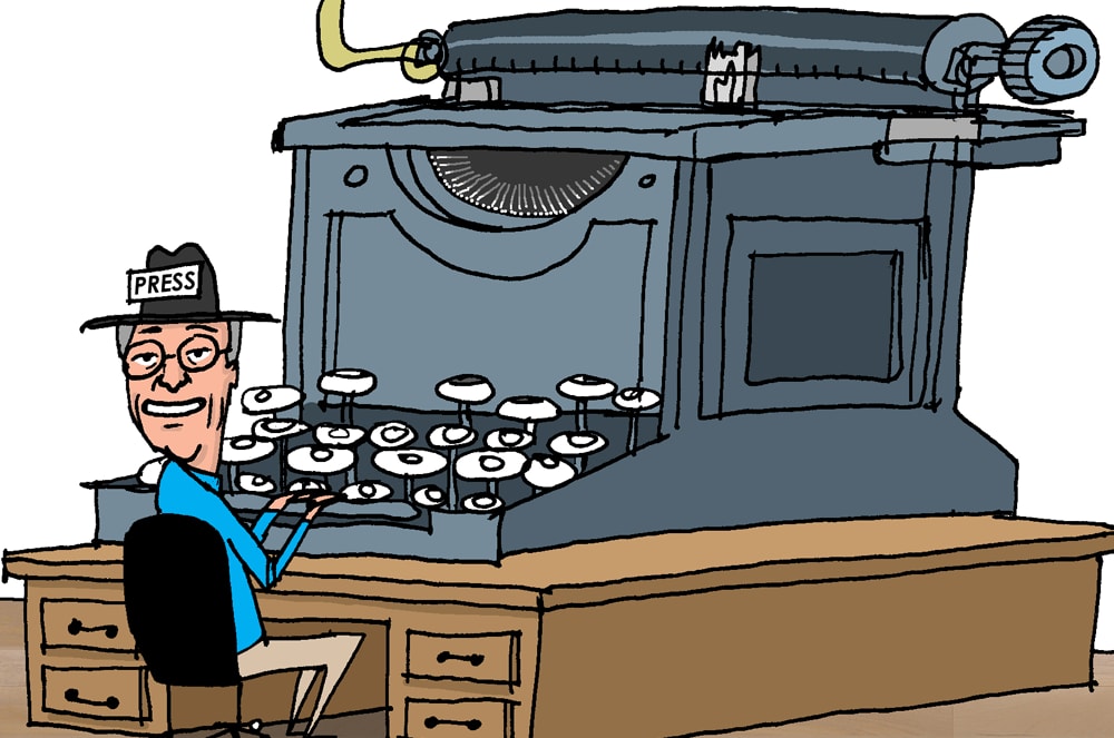 A vintage typewriter sits on a wooden desk, with a smiling man in a hat and suit standing next to it.