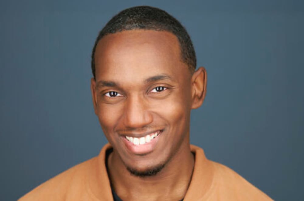 A smiling man with a warm expression against a dark blue background.