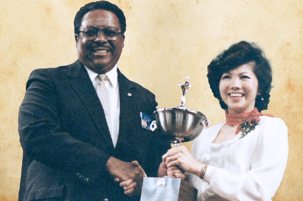The image shows a man and a woman standing together, the man holding a trophy and both of them smiling.
