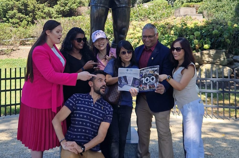 A group of people reading a magazine in front of a statue