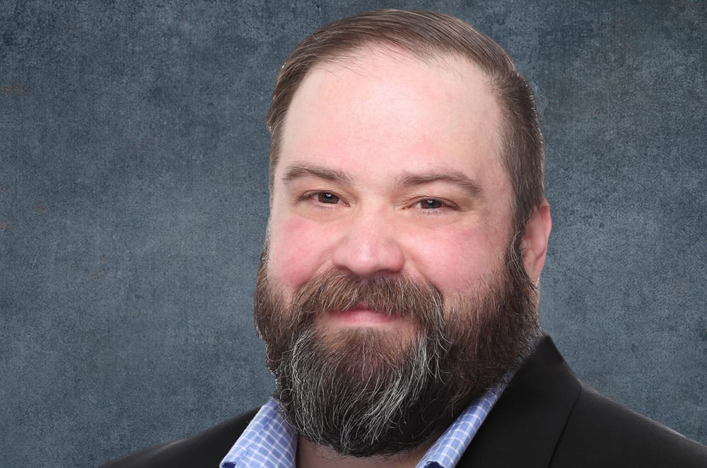 A photo of a smiling man in a white picture frame held up by a blue push pin