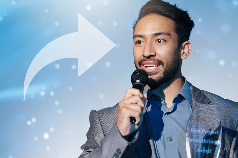 A smiling man in a suit holding a microphone stands in front of a blue background with a white arrow.