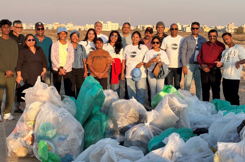 A group of people stand behind a large pile of trash bags in the foreground, with a cityscape in the background.