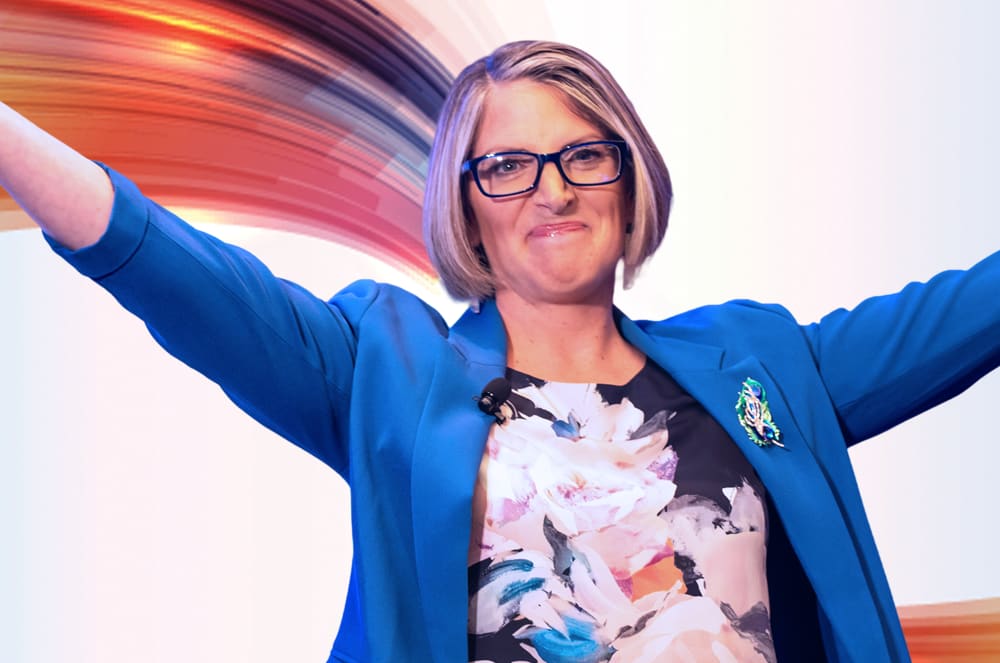 A woman in a blue blazer and floral dress with her arms outstretched stands against a background of colorful abstract lines.