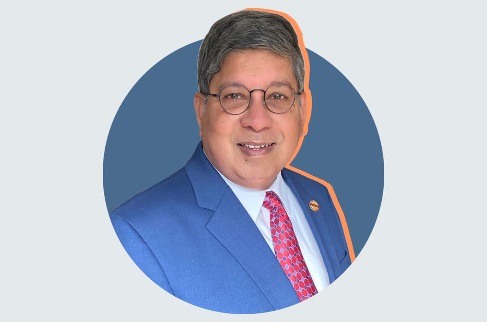 A man in a blue suit and red tie smiles from within a blue circle against a light gray and orange background.