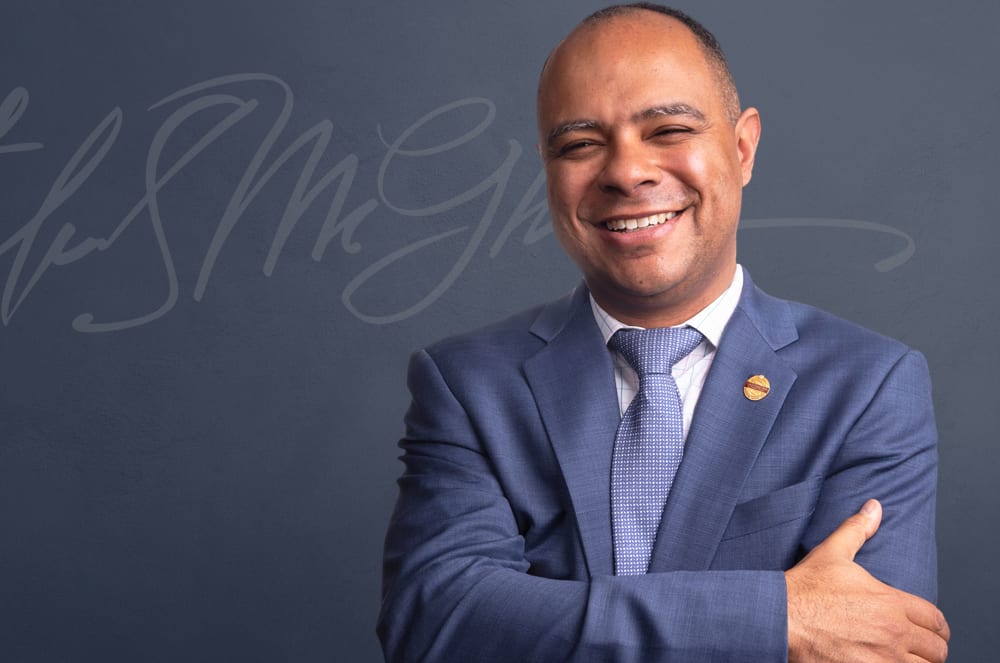 A man wearing a suit and tie smiles and crosses him arms