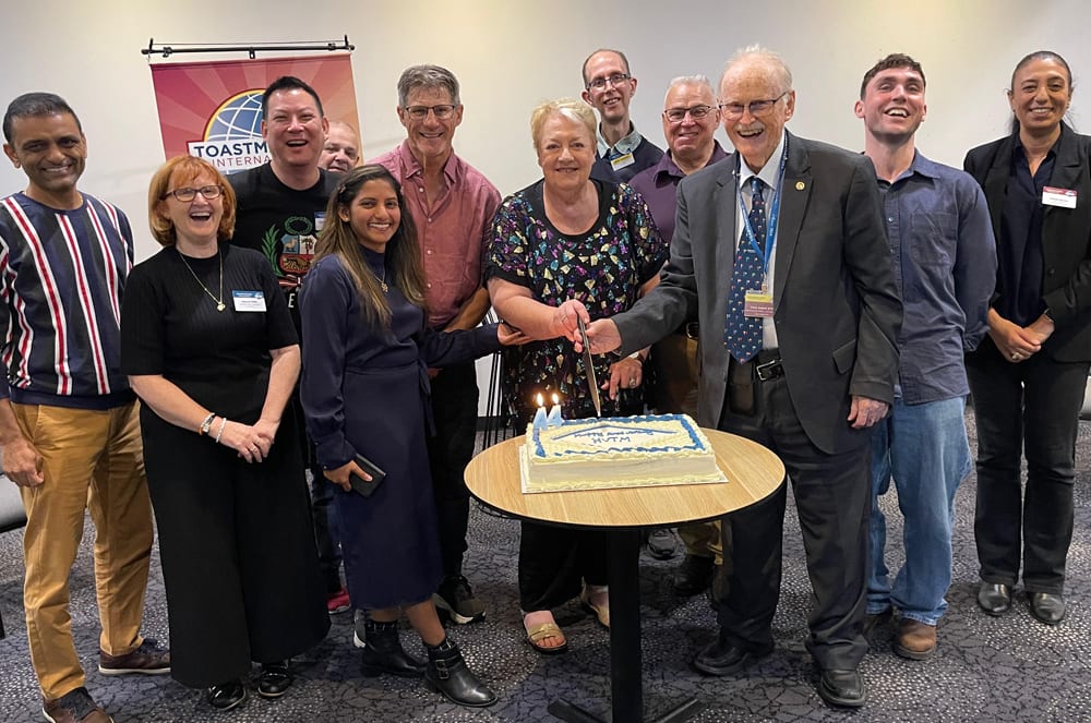 A group of people laughing and standing around a table with a cake on it