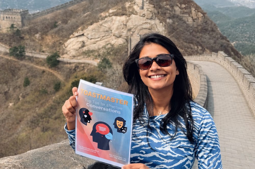 A smiling woman wearing sunglasses holds a magazine while standing on the Great Wall of China
