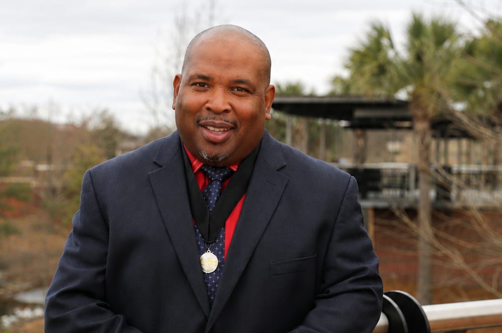 A smiling man wearing a black suit and a silver medal