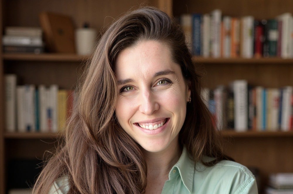A smiling woman wearing a green button-up shirt standing in front of a bookshelf