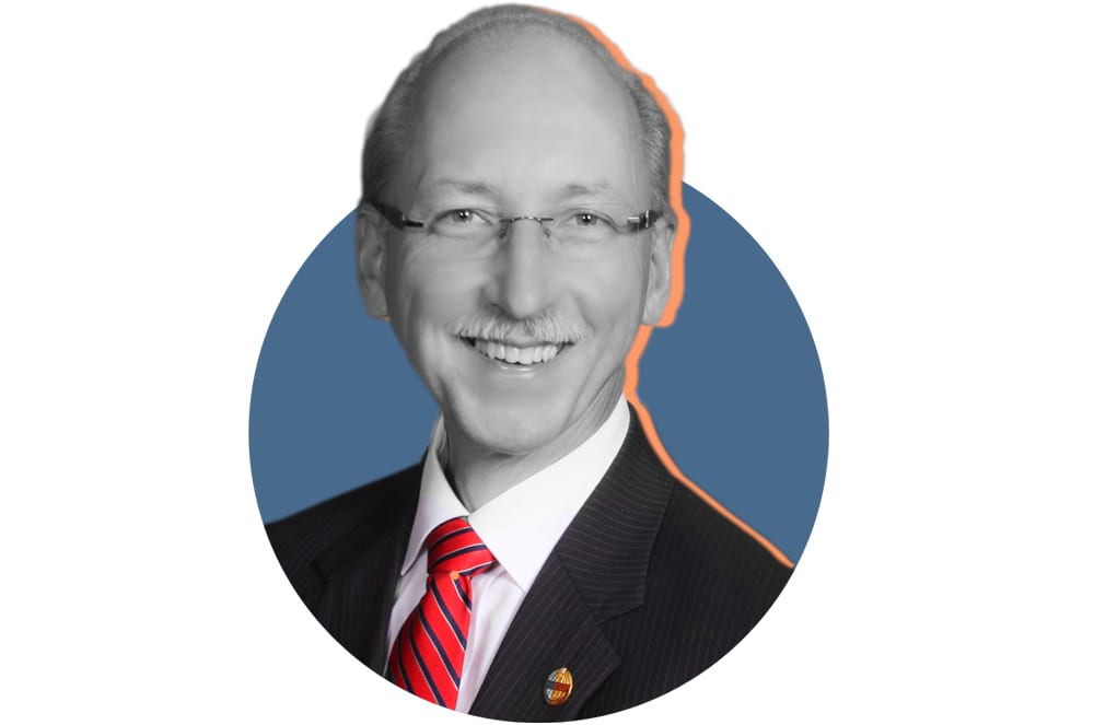 A smiling man wearing a black suit and red tie