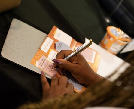 A person's hands are writing on a notebook with sticky notes and a pen, against a dark background.
