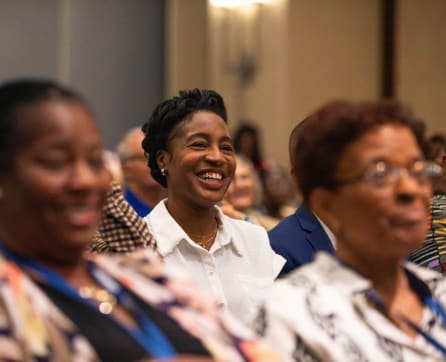The image shows a group of smiling African American women seated together, appearing to be engaged in a conversation or event.