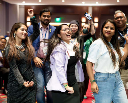 A group of smiling and enthusiastic people gathered in what appears to be a conference or event setting, with a colorful and vibrant background.